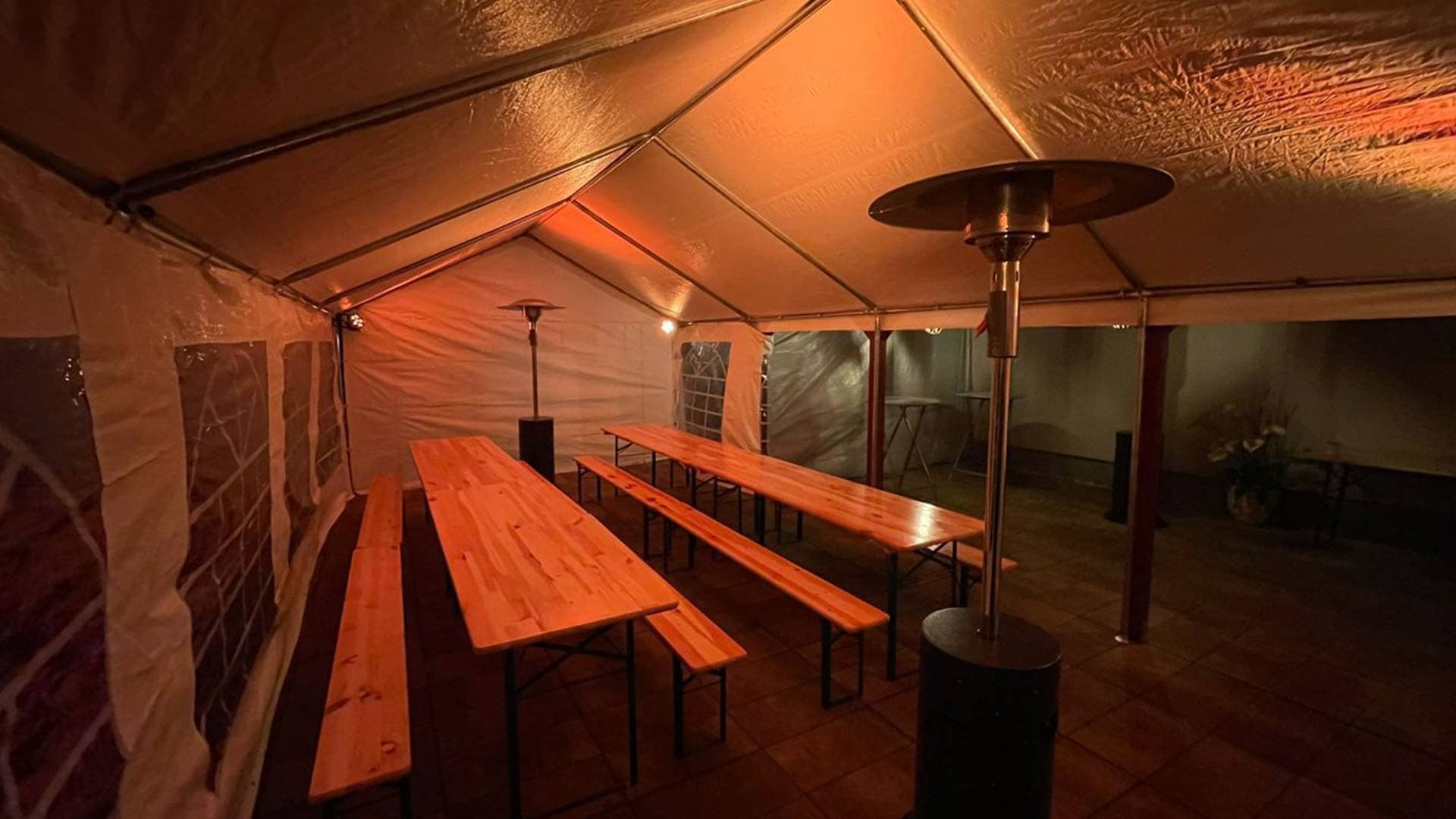 Innenansicht eines beheizten Festzelts mit langen Holztischen, Bänken und Heizstrahlern bei abendlicher Beleuchtung